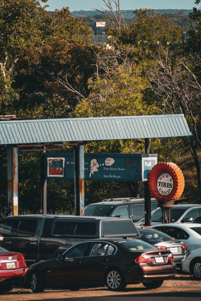 A parked car lot with a used tire shop surrounded by lush trees in autumn.