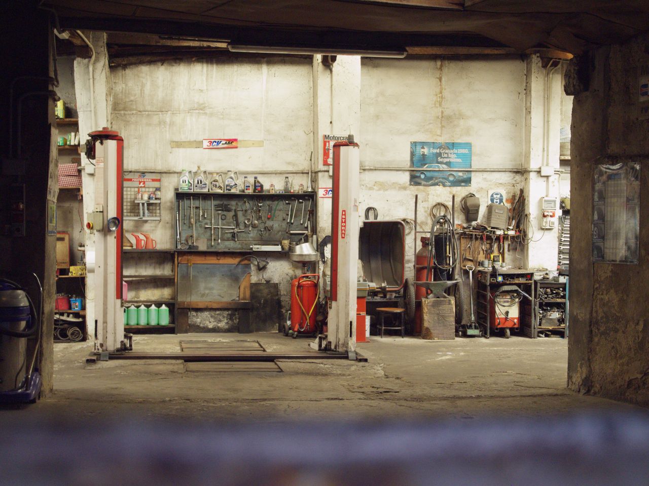 An empty, rustic car workshop featuring tools, machinery, and car lifts in an industrial setting.